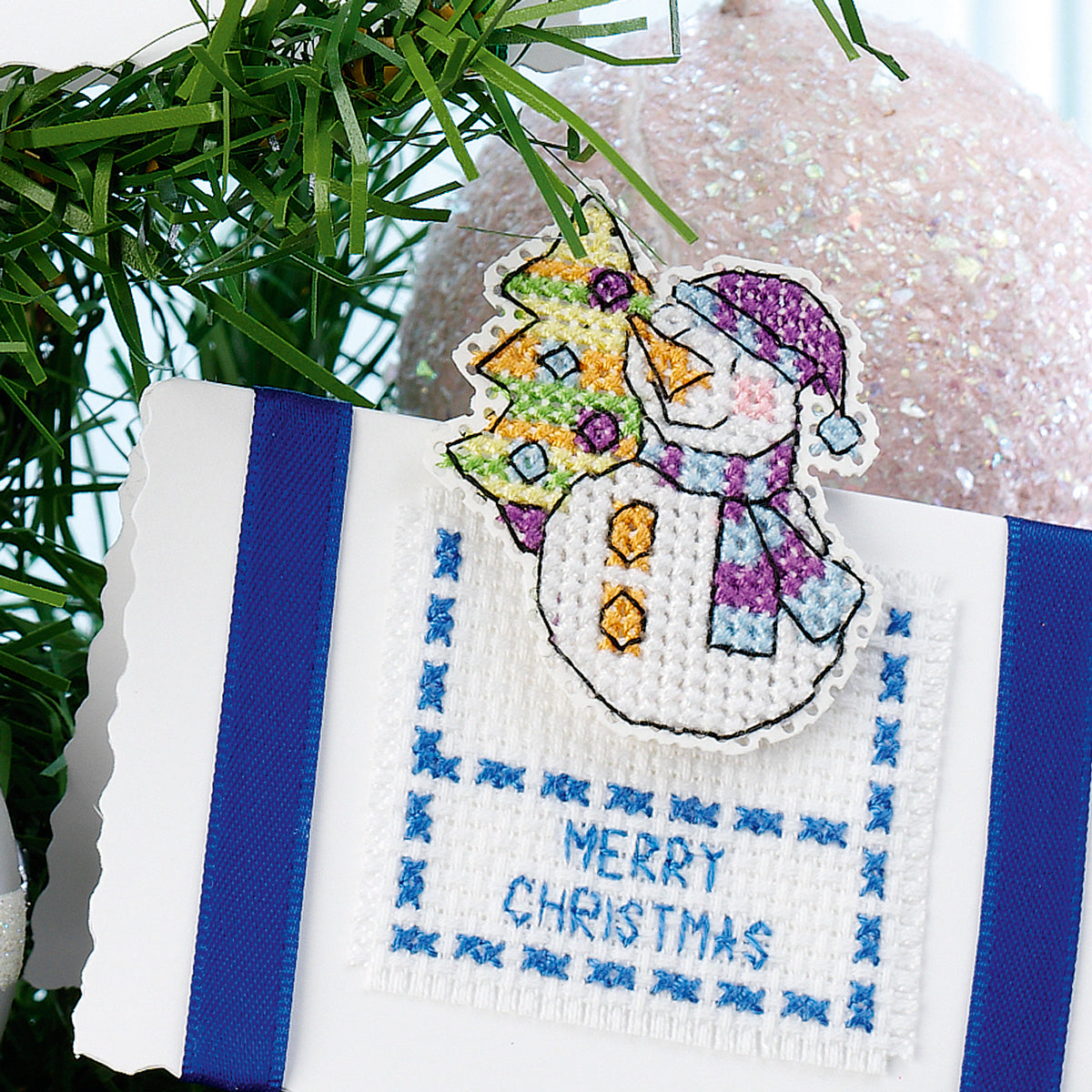 Cross-stitched snowman ornament with 'Merry Christmas' text on a white background.