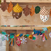 Two decorative garlands on a wooden surface, one with autumn-themed elements and the other with colorful flowers and tassels.