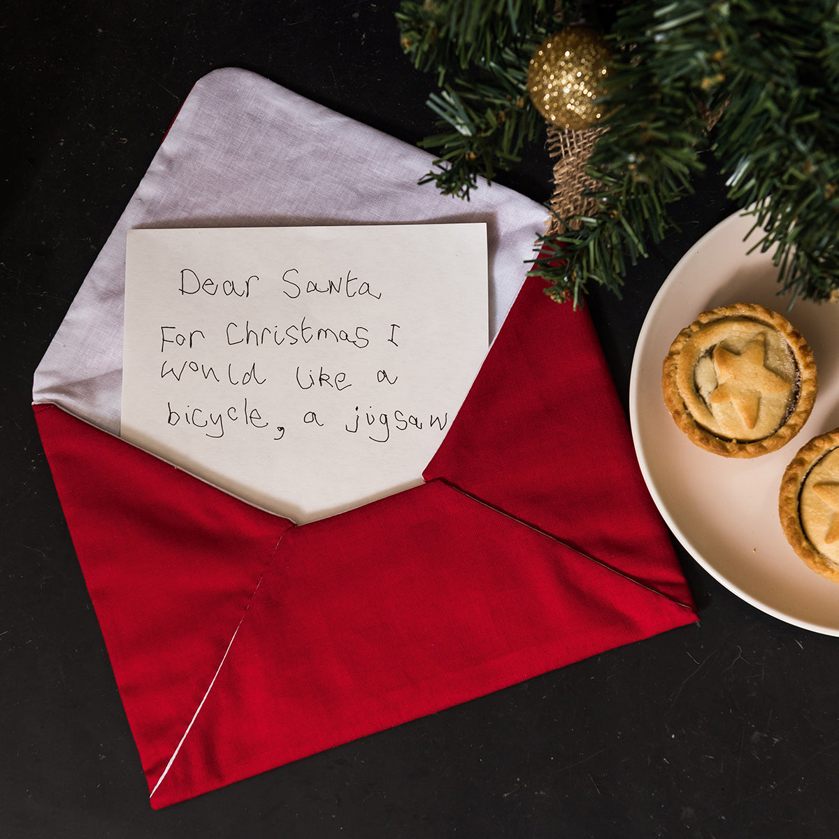 Letter to Santa on a red envelope with Christmas decorations and pastries.