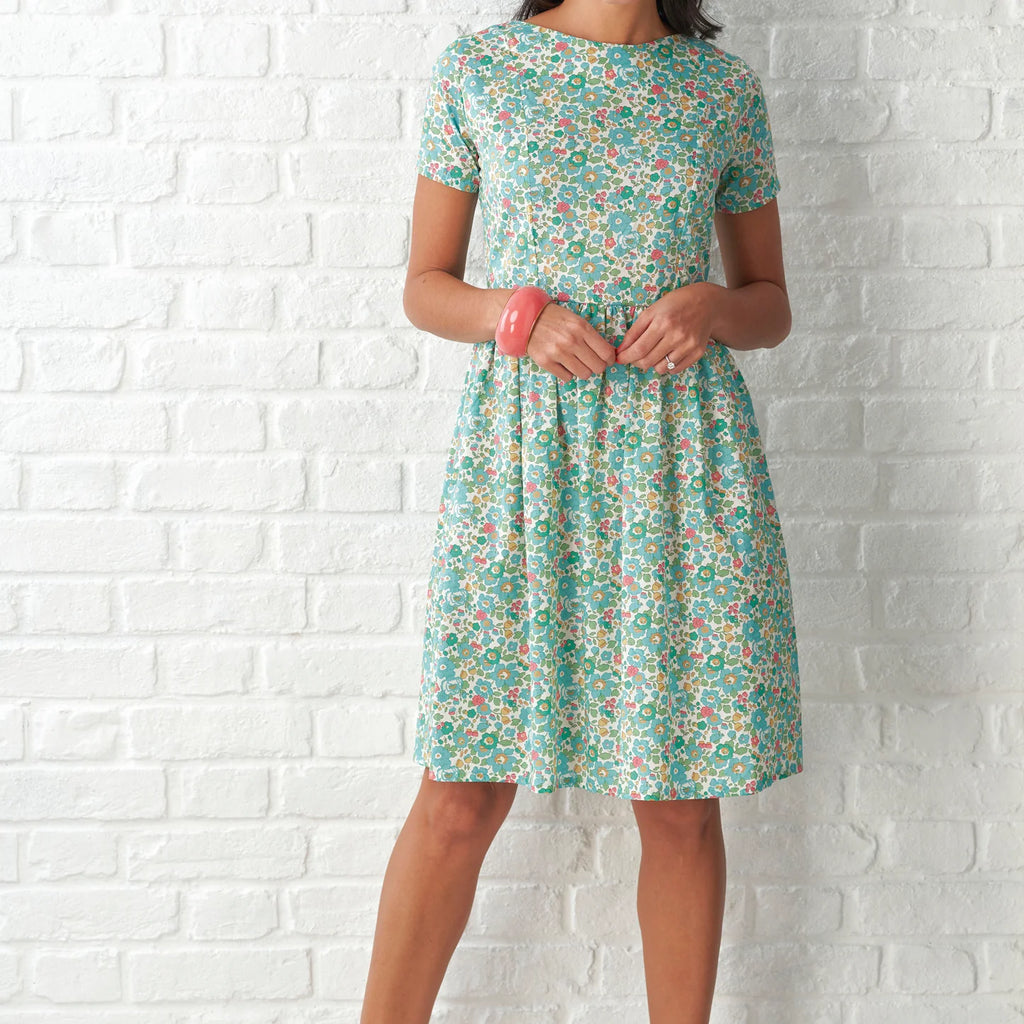 Woman wearing a floral dress against a white brick wall