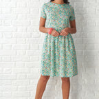 Woman wearing a floral dress against a white brick wall