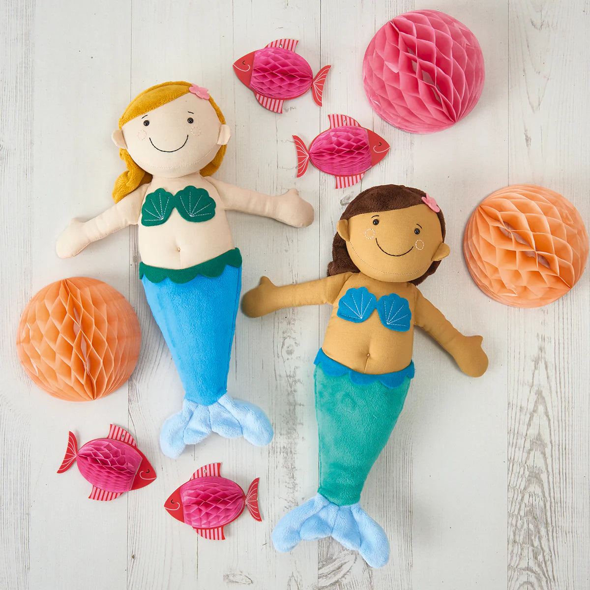 Two mermaid dolls with colorful fish and honeycomb decorations on a light wooden surface.