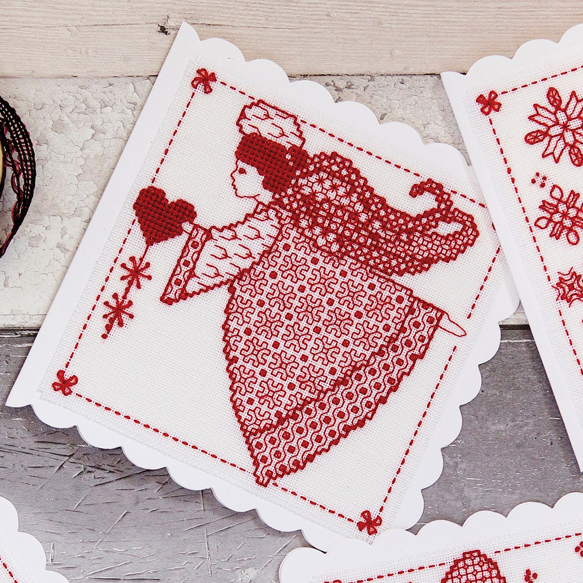 Cross stitch fabric with a red design of a child holding a heart on a white background.