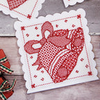 Cross stitch red design on a white fabric with decorative edges on a wooden surface.