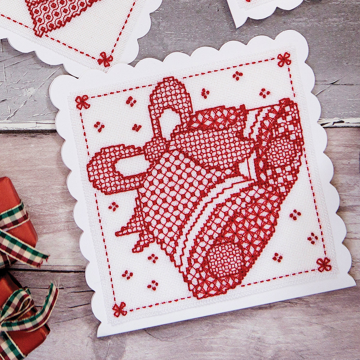 Cross stitch red design on a white fabric with decorative edges on a wooden surface.