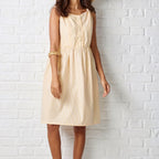 Woman wearing a beige dress against a white brick wall