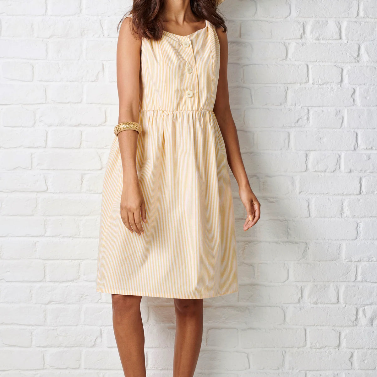 Woman wearing a beige dress against a white brick wall