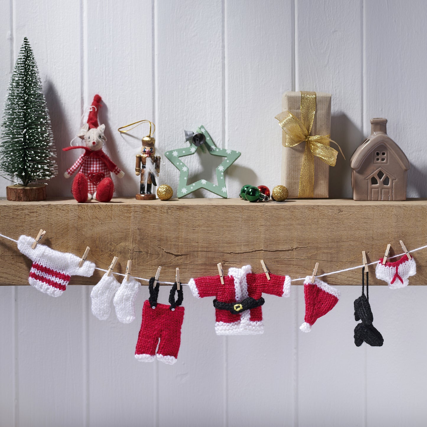 Knitted Santa Claus outfit on a clothesline with Christmas decorations in the background.