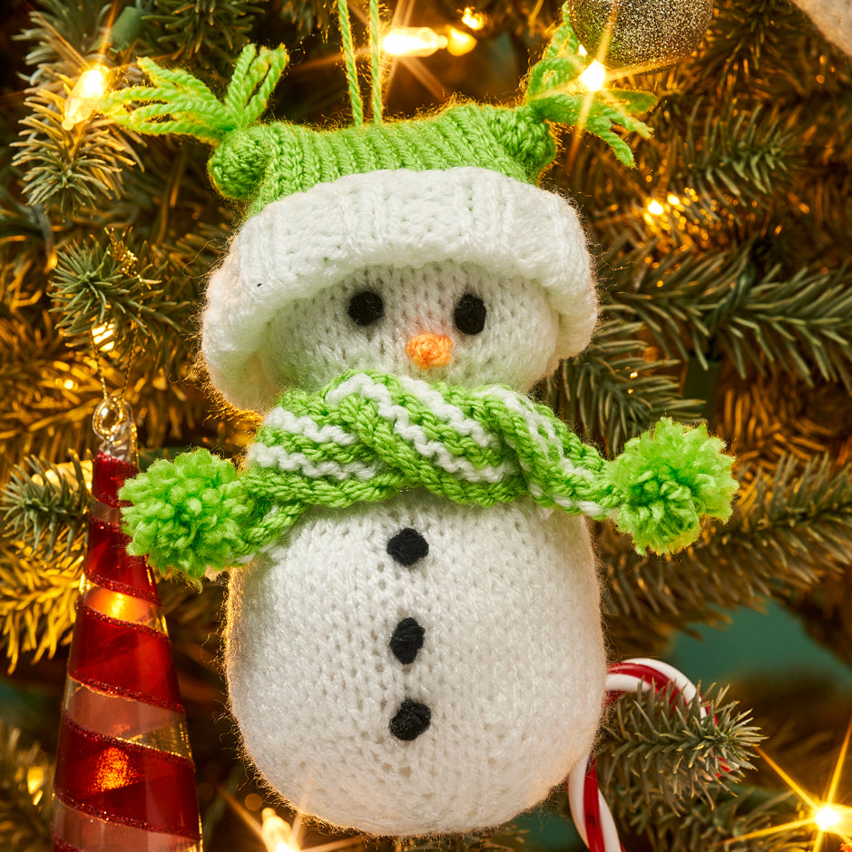 Knitted snowman ornament with green scarf and hat on a Christmas tree.