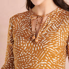 Close-up of a person wearing a patterned brown and white blouse with a necklace.