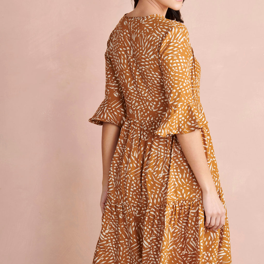 Woman wearing a brown and yellow patterned dress against a beige background