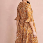 Woman wearing a brown and yellow patterned dress against a beige background