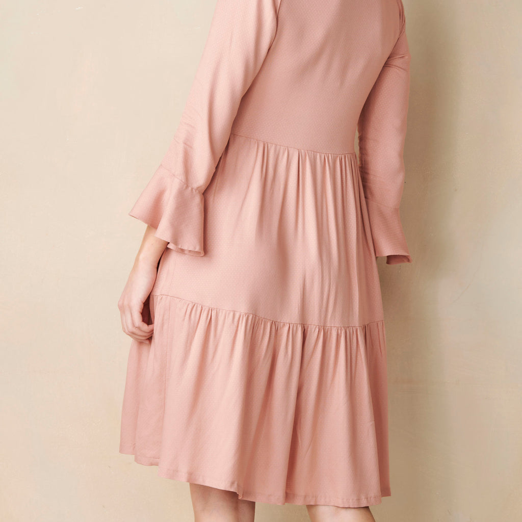 Pink dress with ruffled sleeves and hem on a beige background