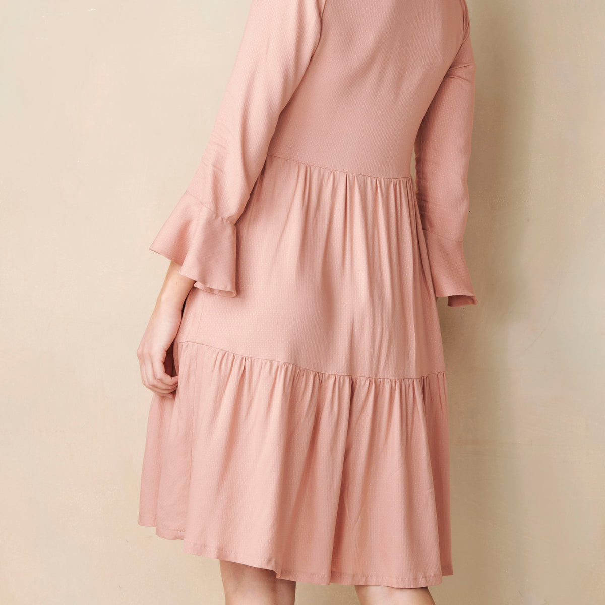 Pink dress with ruffled sleeves and hem on a beige background