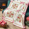 Quilt with floral pattern on a couch next to a fireplace and gift boxes.