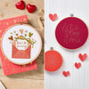 Embroidery hoops with love-themed designs and red hearts on a wooden surface.