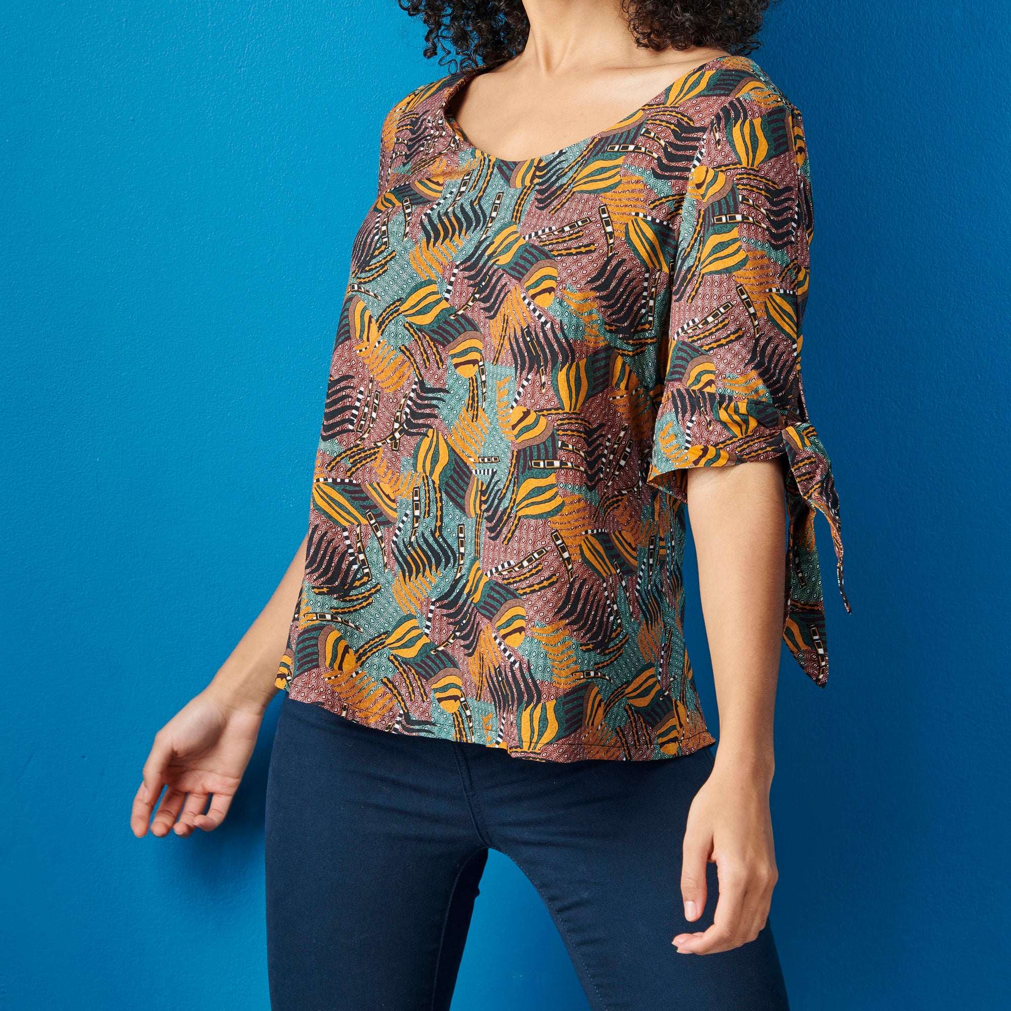 Woman wearing a patterned top and dark pants against a blue background