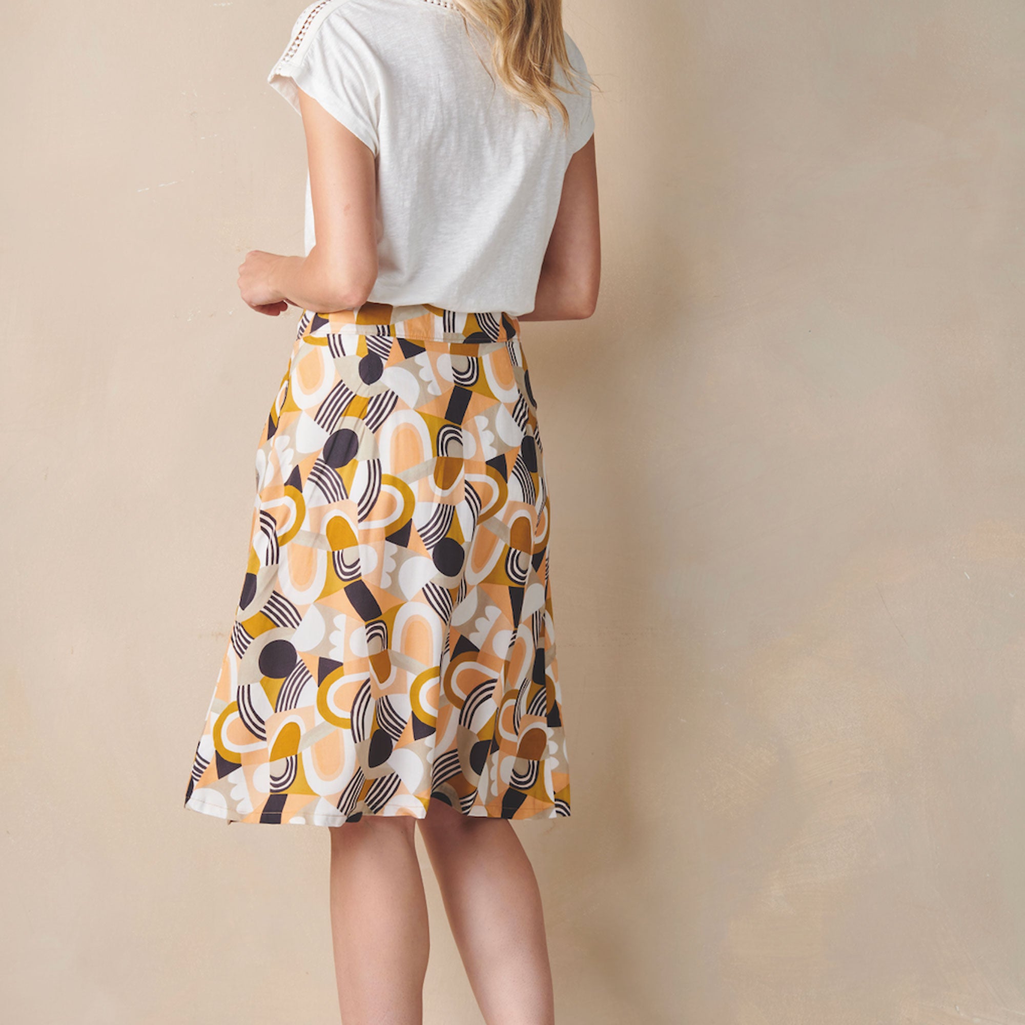 Woman wearing a white top and patterned skirt on a beige background