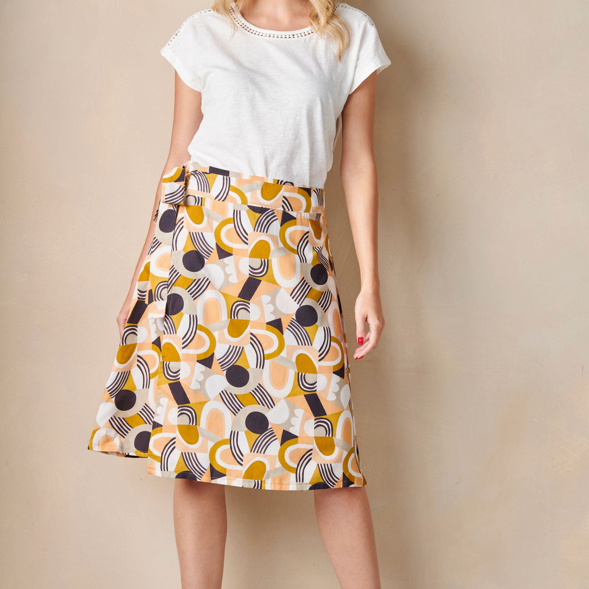 Woman wearing a white top and patterned skirt against a beige background